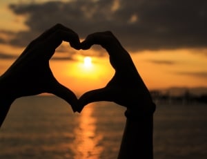 silhouette of person forming heart sign using hands during golden hour thumbnail