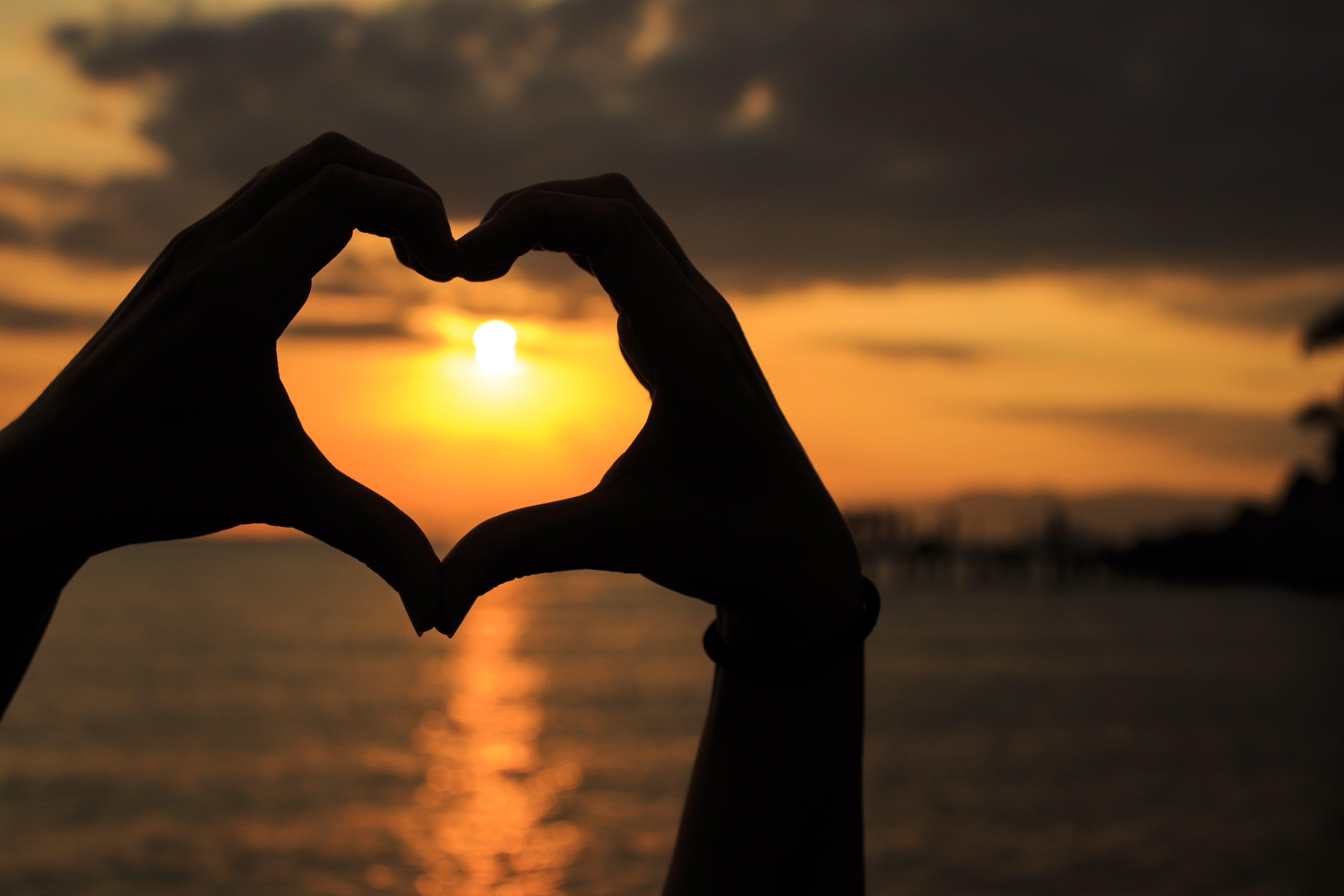 silhouette of person forming heart sign using hands during golden hour