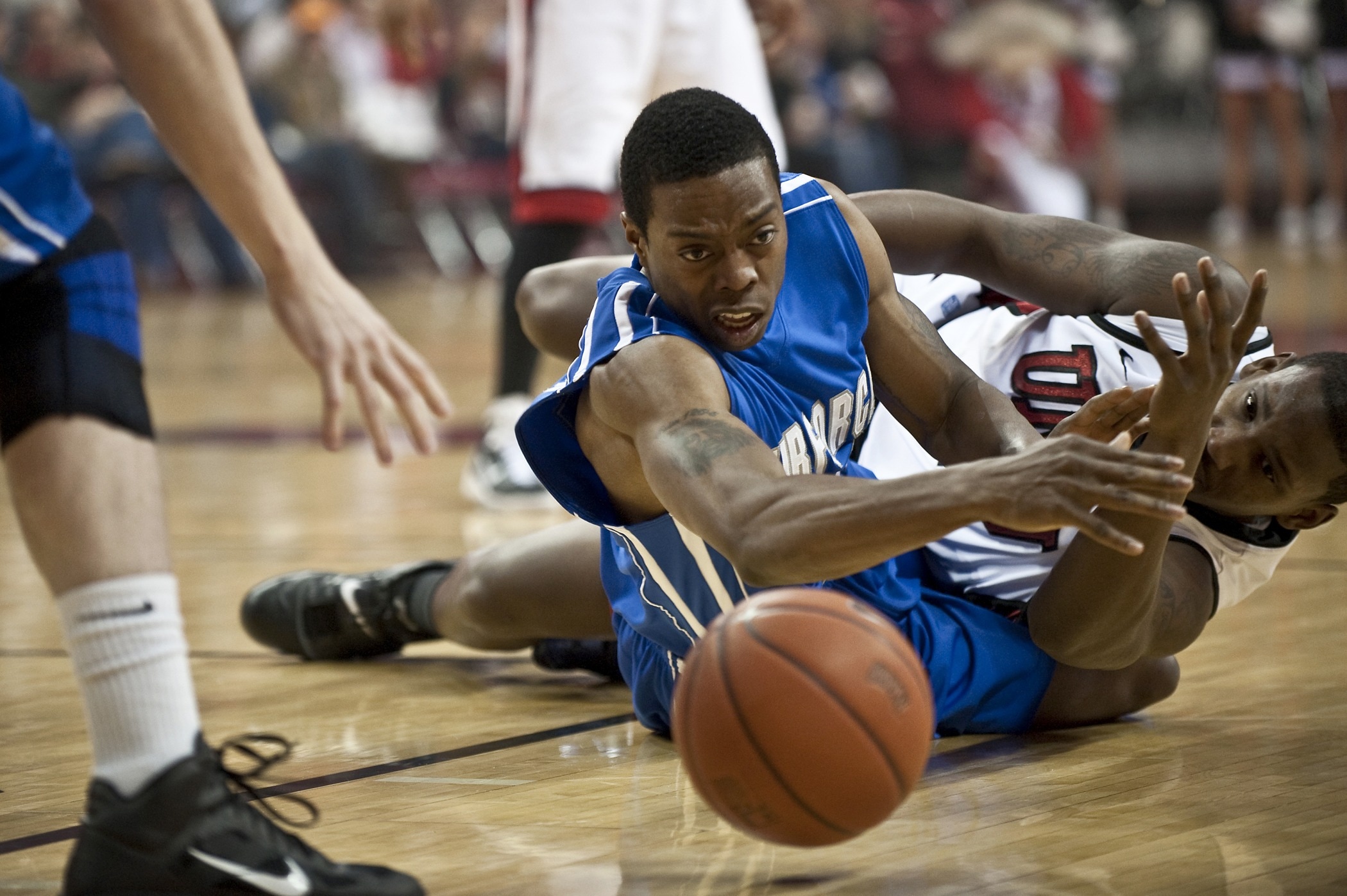 two opposing basketball players diving for the ball