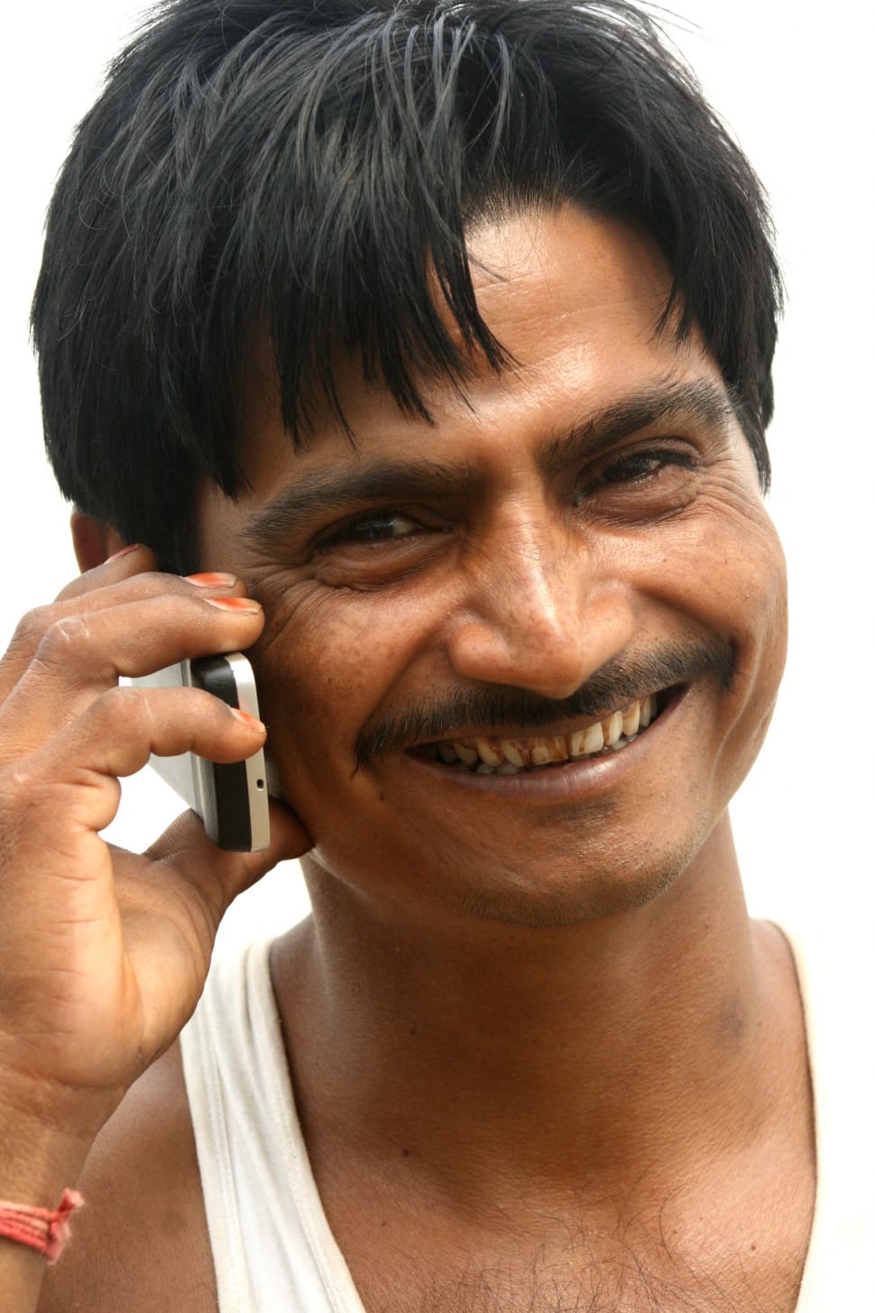 man wearing white tank top holding white and black candybar phone preview