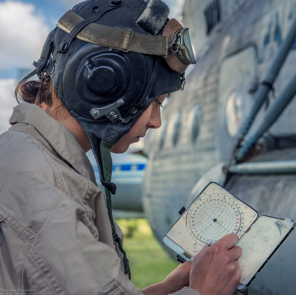 man in black aviator helmet looking at book near plane preview