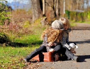 two girls sitting on brown suitcase thumbnail