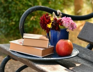 red apple fruit and red pink and yellow floral bouquet and 2 books thumbnail