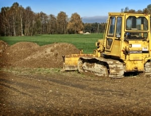 yellow front loader truck on brown soil next to green grass thumbnail