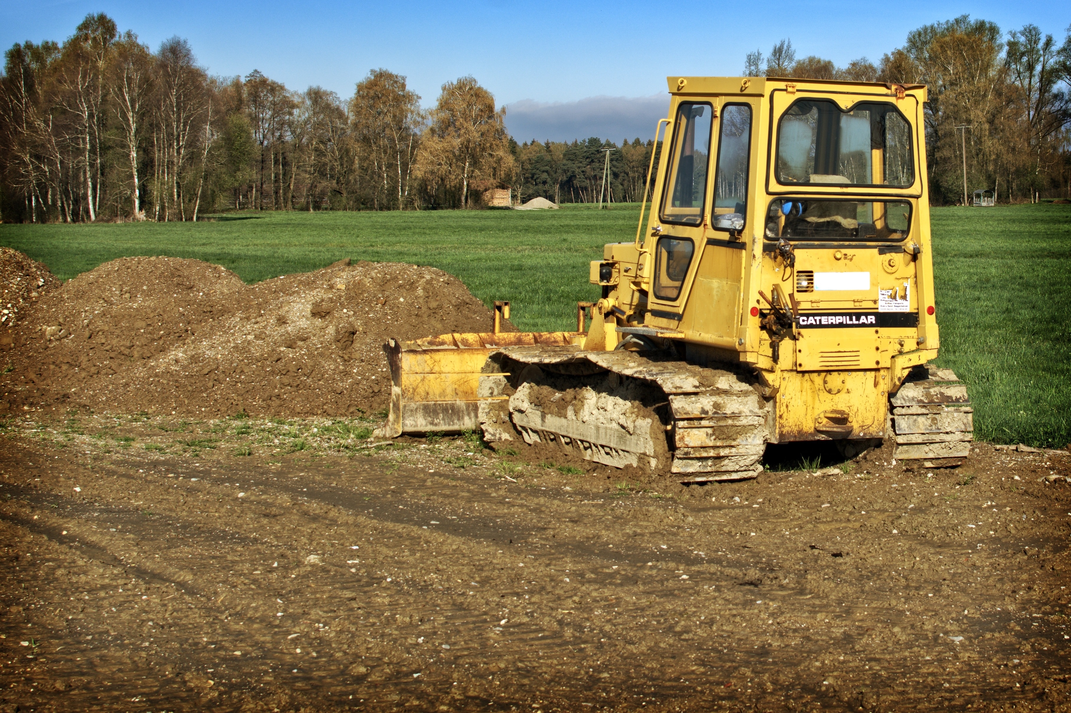 yellow front loader truck on brown soil next to green grass