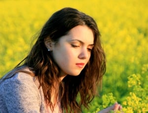 woman in gray shirt sitting on yellow flower fields at daytime thumbnail
