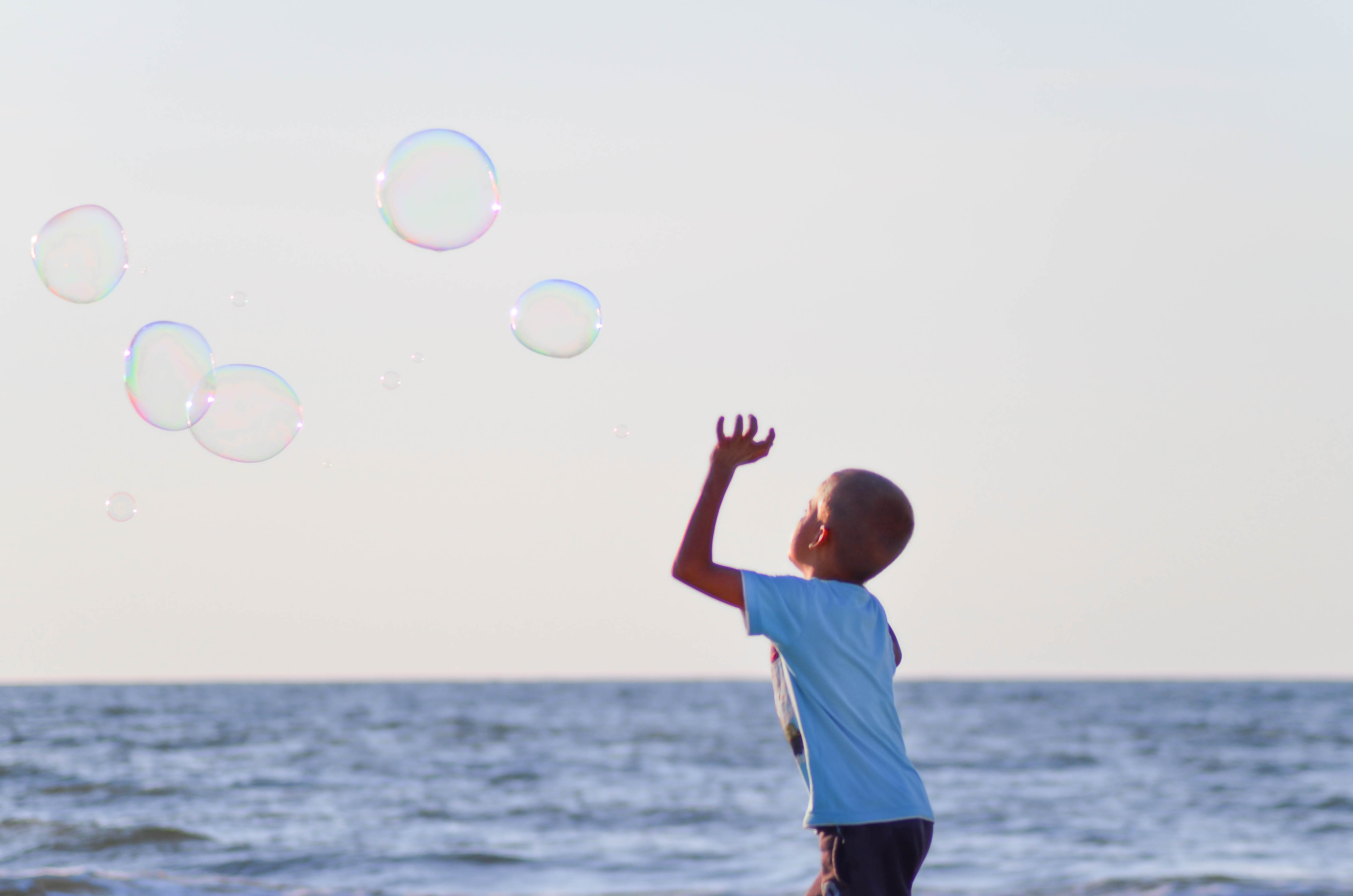 boy playing bubbles near body of water during daytime