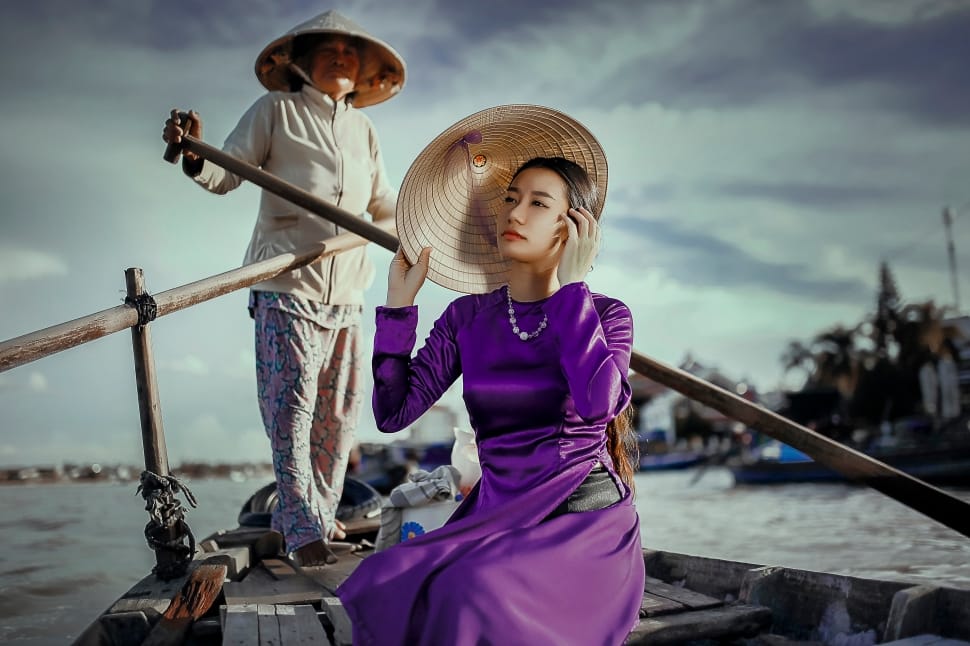 man paddling the boat while woman riding in purple long sleeve dress and holding brown hat preview