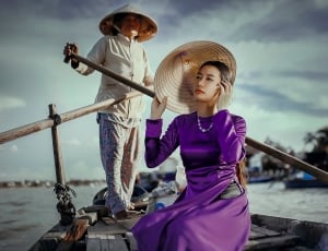 man paddling the boat while woman riding in purple long sleeve dress and holding brown hat thumbnail