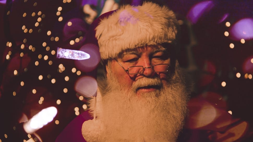 santa claus wearing eyeglasses standing beside pink surface with bokeh lights preview