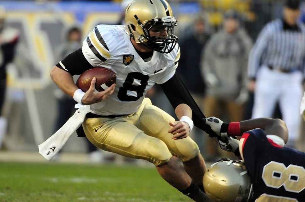football player in complete football gear holding a football while dodging an opponent preview