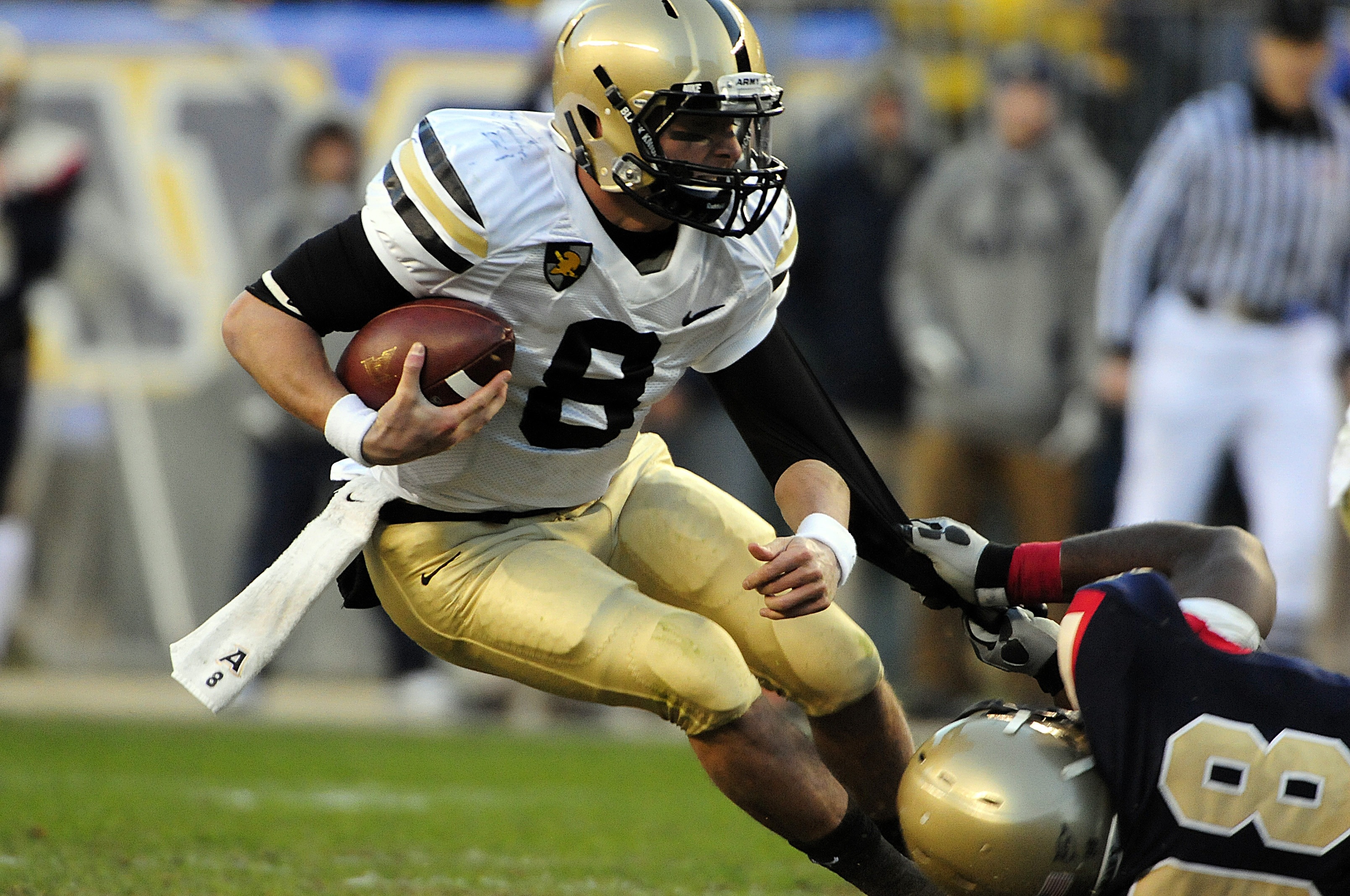 football player in complete football gear holding a football while dodging an opponent