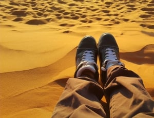 person wearing brown pants and black lace up sneakers in dessert thumbnail