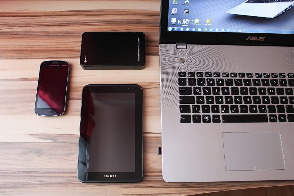 a picture of grey and black asus laptop, samsung computer tablet. and two android smartphones on top of brown wooden table free image - Peakpx