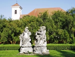 two brown concrete statues on near green trees at daytime thumbnail
