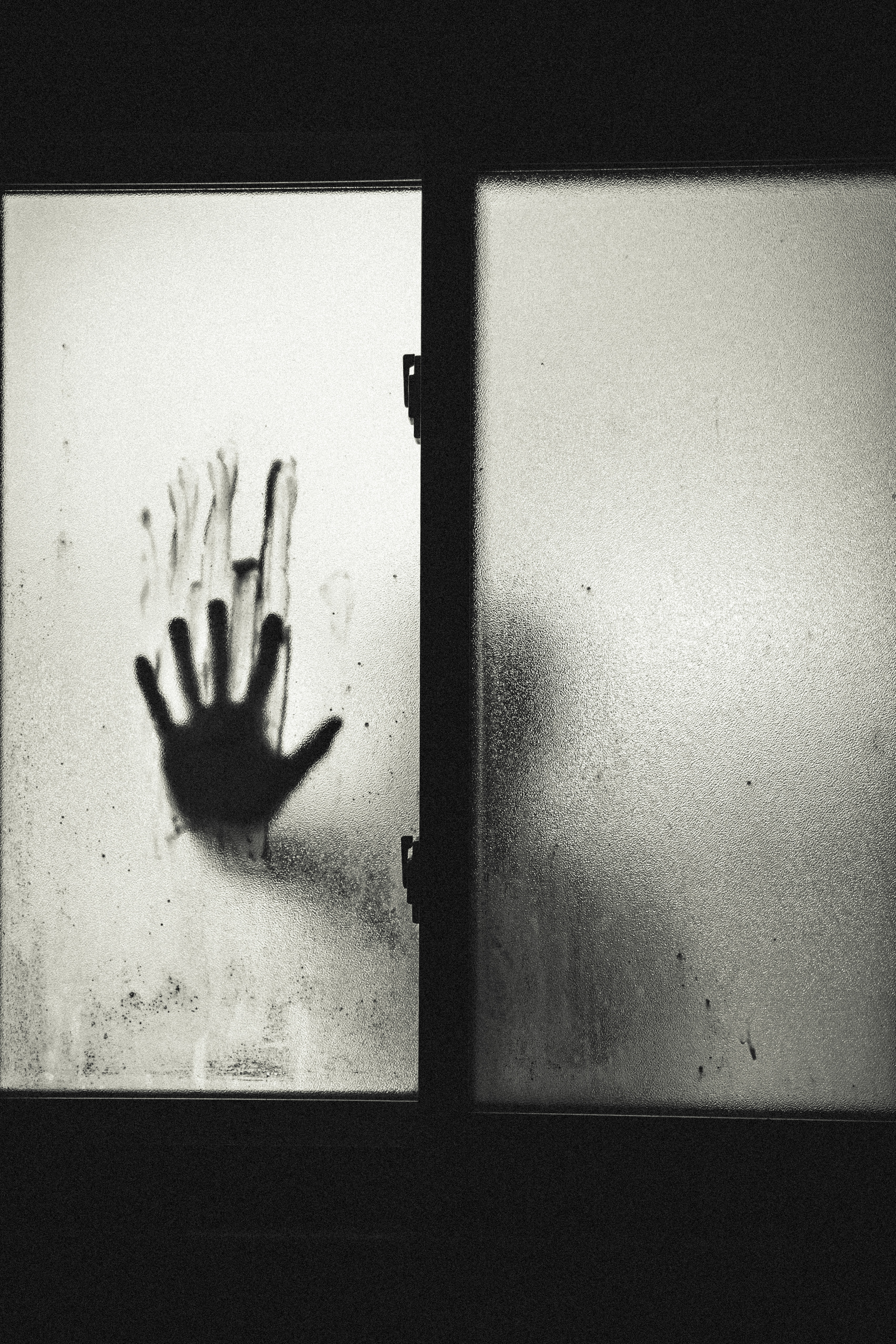 grayscale photo of a person with right stained hand on glass window