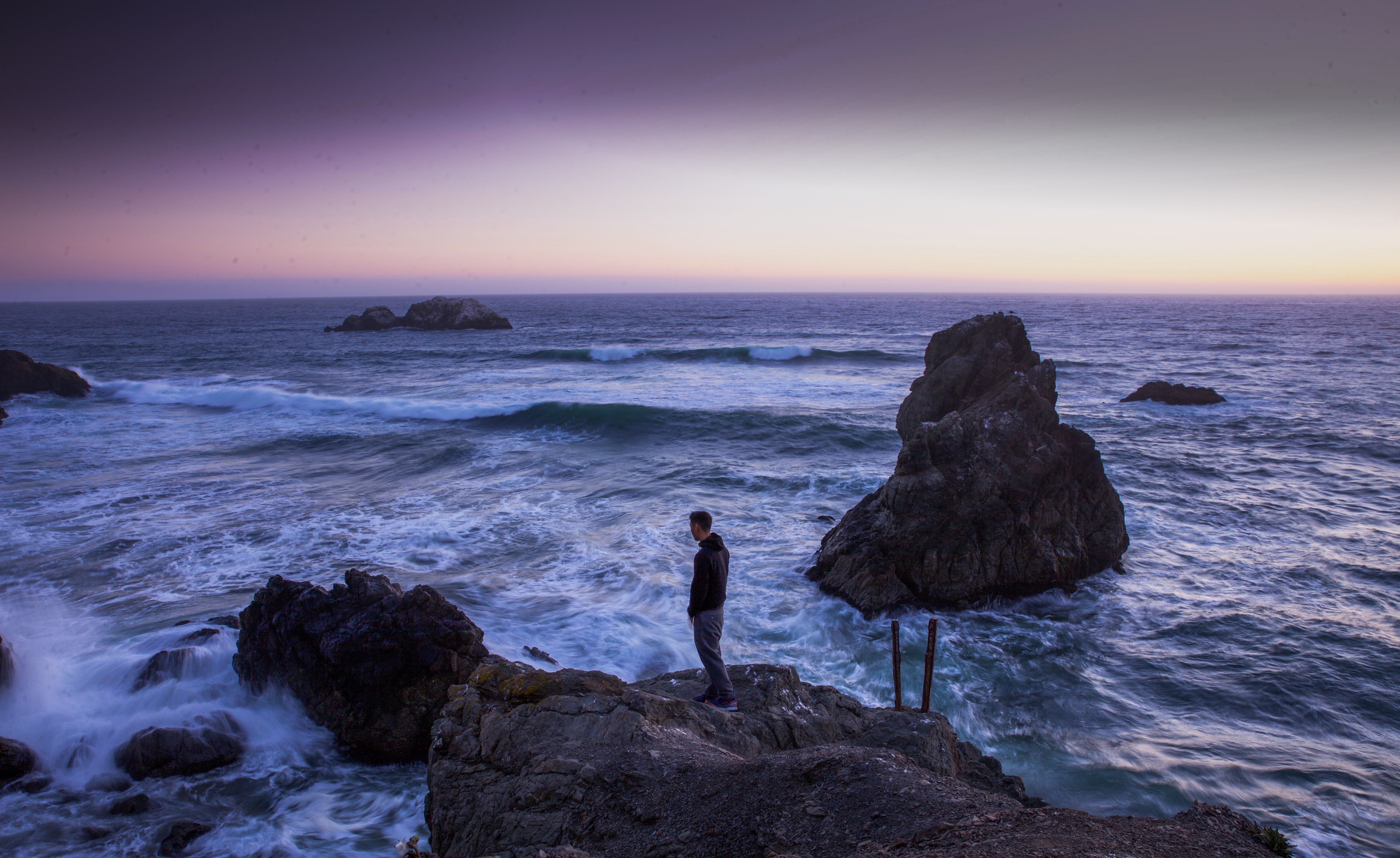 man in black leather jack standing on rock near sea