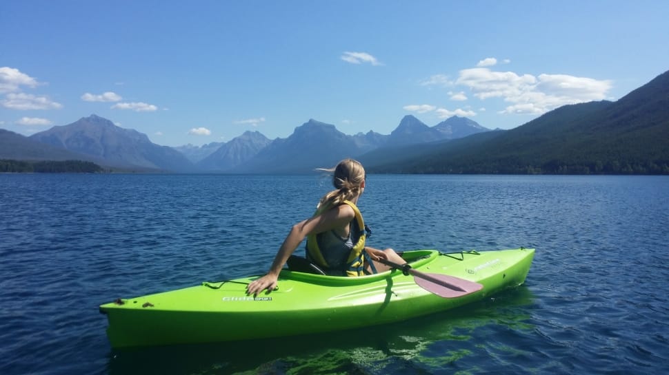 woman riding on green kayak near mountains during daytime preview