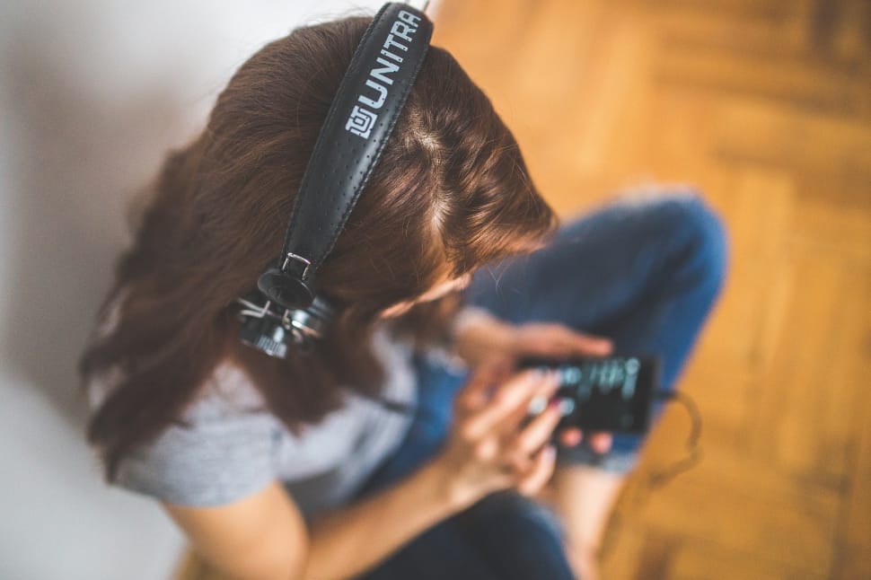 Young woman wearing headphones, holding mobile phone and listening to music preview
