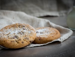 two brown cookies with white powder on beige textile thumbnail