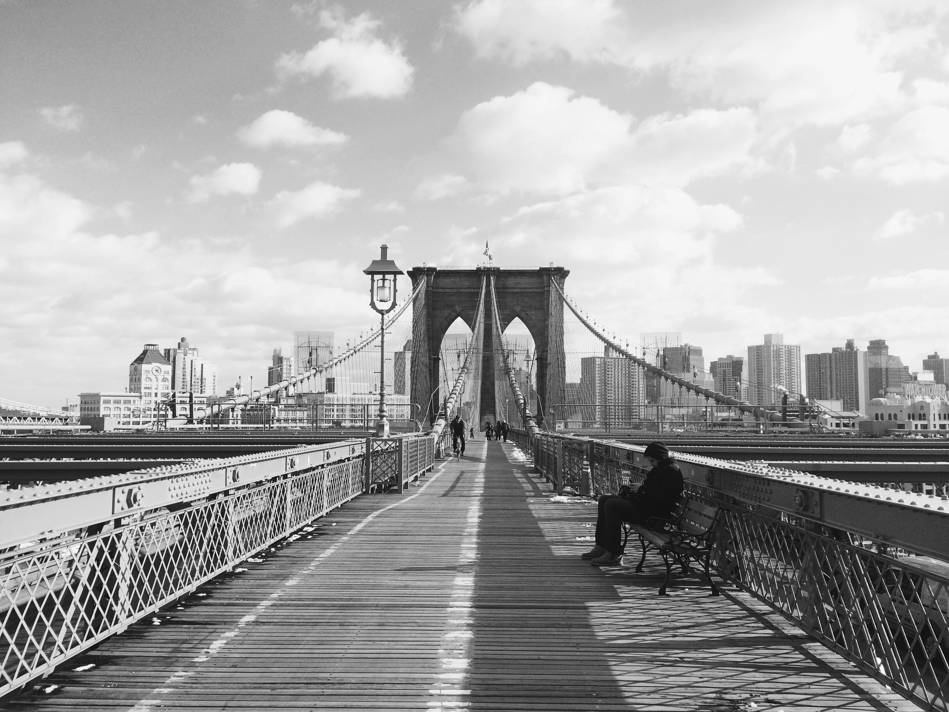 grayscale photo of man sitting on bench on bridge