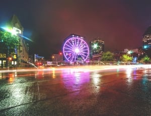 purple lighted Ferris wheel beside buildings and lighted fountain during nighttime thumbnail