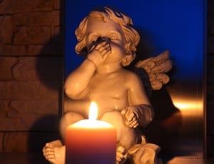 lighted candle in front of cherub ceramic figurine inside room thumbnail