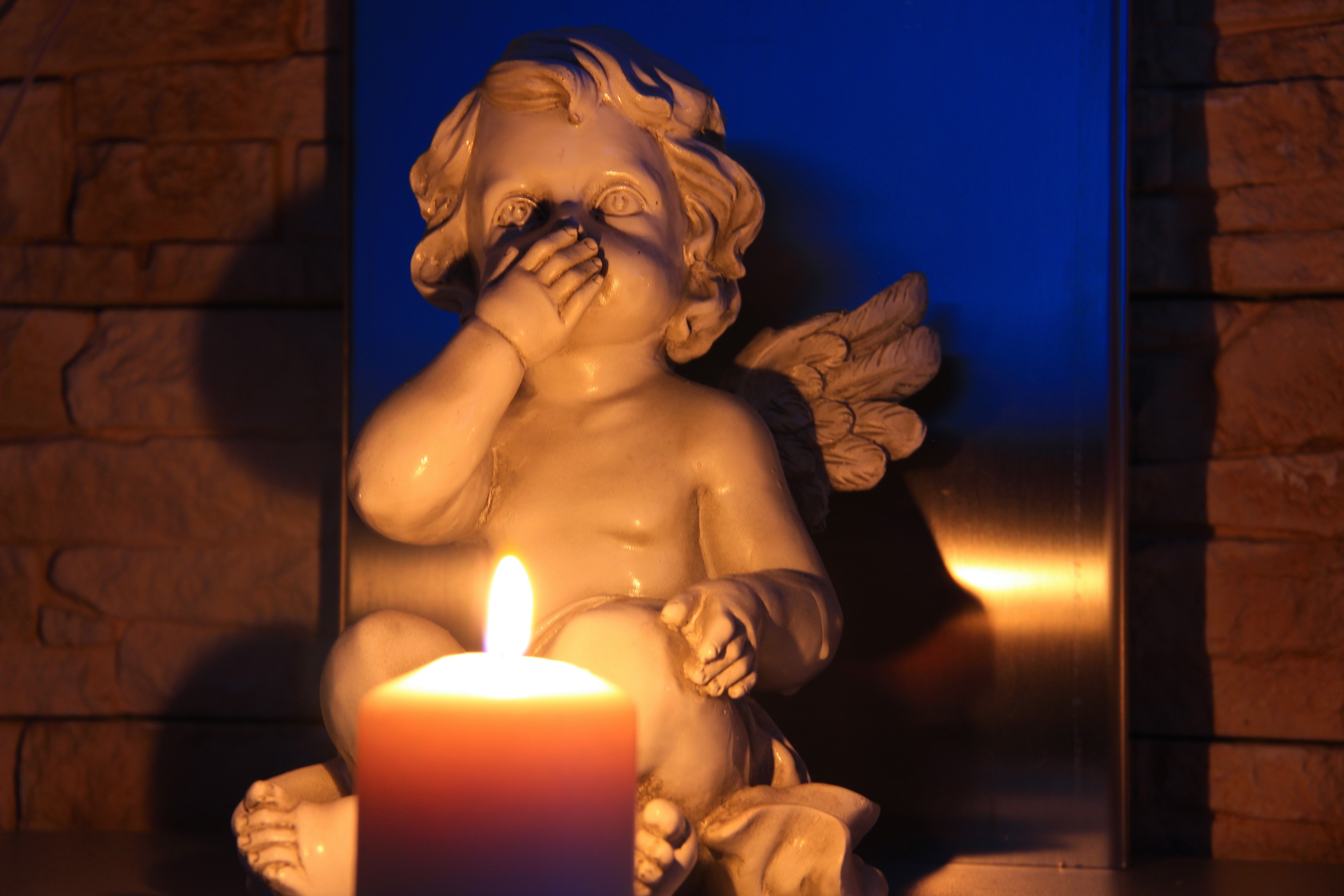 lighted candle in front of cherub ceramic figurine inside room