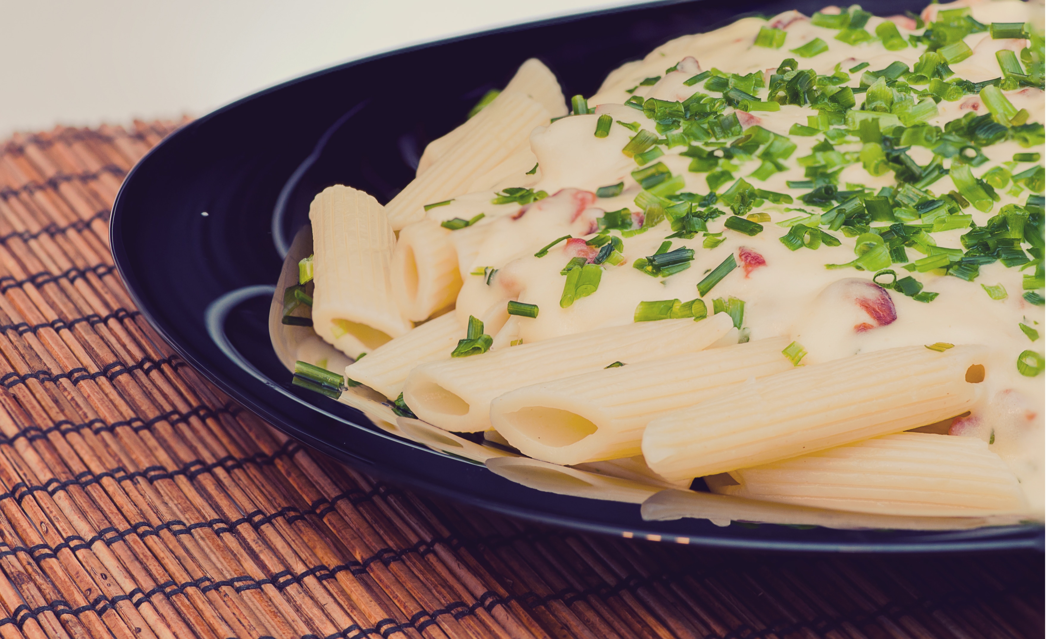 penne pasta dish with white sauce on top and chopped vegetalbe