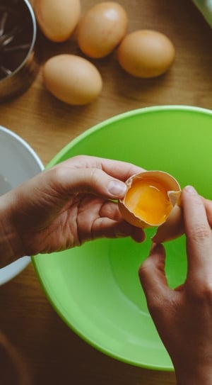 person holding cracked egg on top of bowl thumbnail