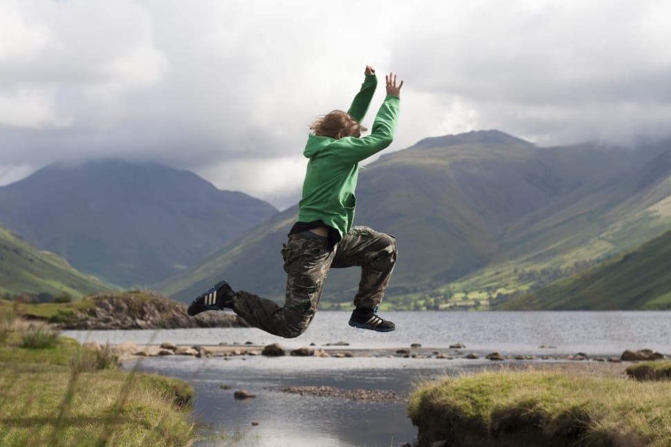 person in green hoodie, brown and gray camouflage pants and black adidas sneakers jumping from cliff to cliff photo preview