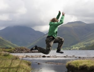 person in green hoodie, brown and gray camouflage pants and black adidas sneakers jumping from cliff to cliff photo thumbnail