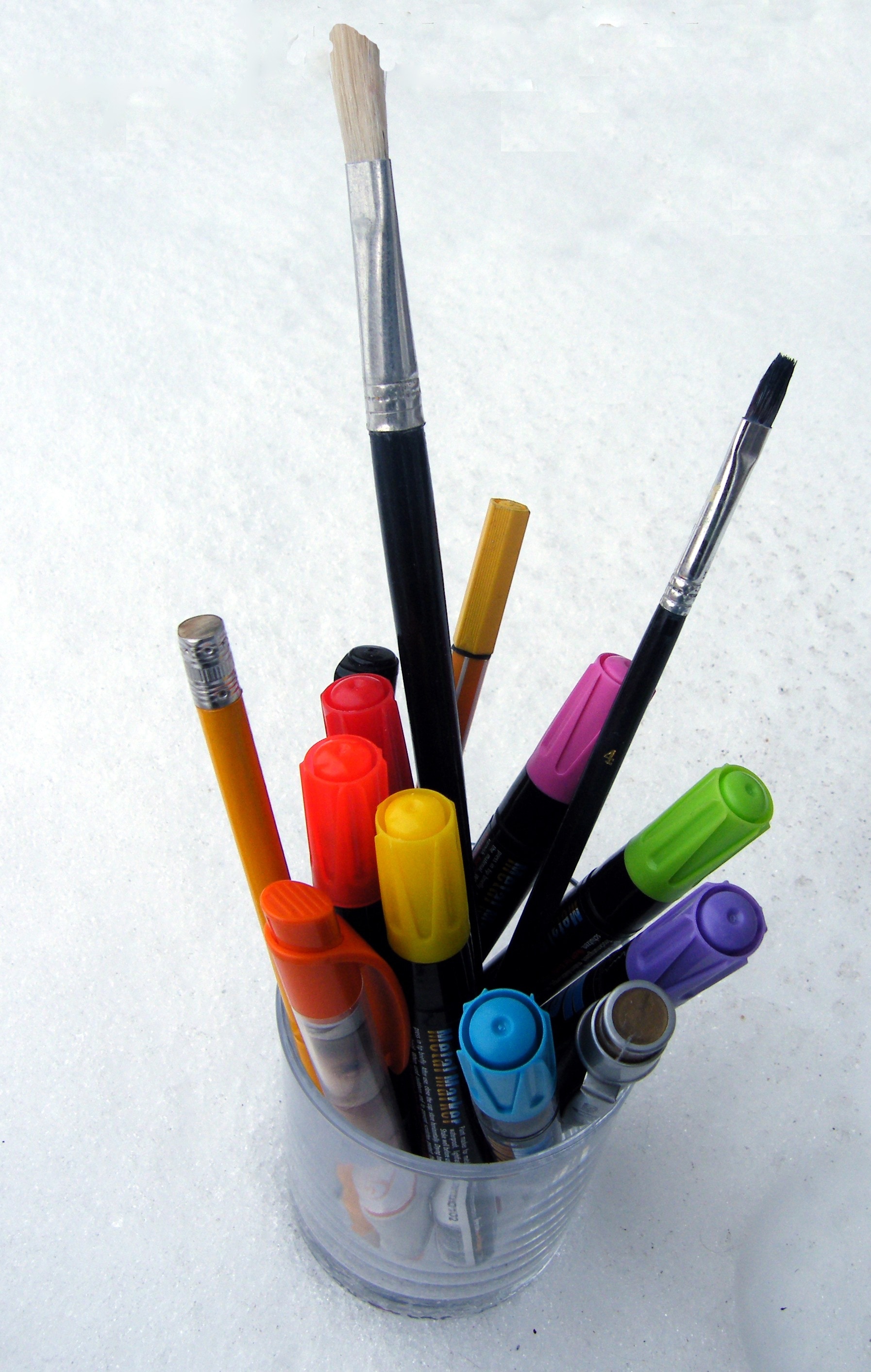 assorted markers and paintbrush in plastic cup