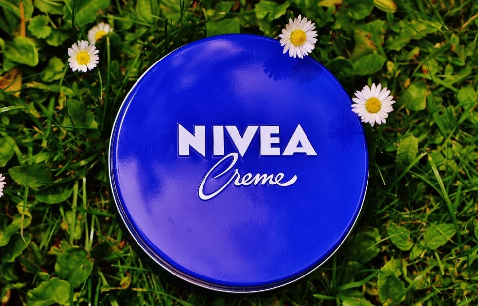 blue nvea creme metal container on green leaf with four white daisy flowers preview