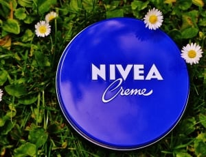blue nvea creme metal container on green leaf with four white daisy flowers thumbnail