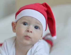 baby in red santa claus hat laying on bed thumbnail