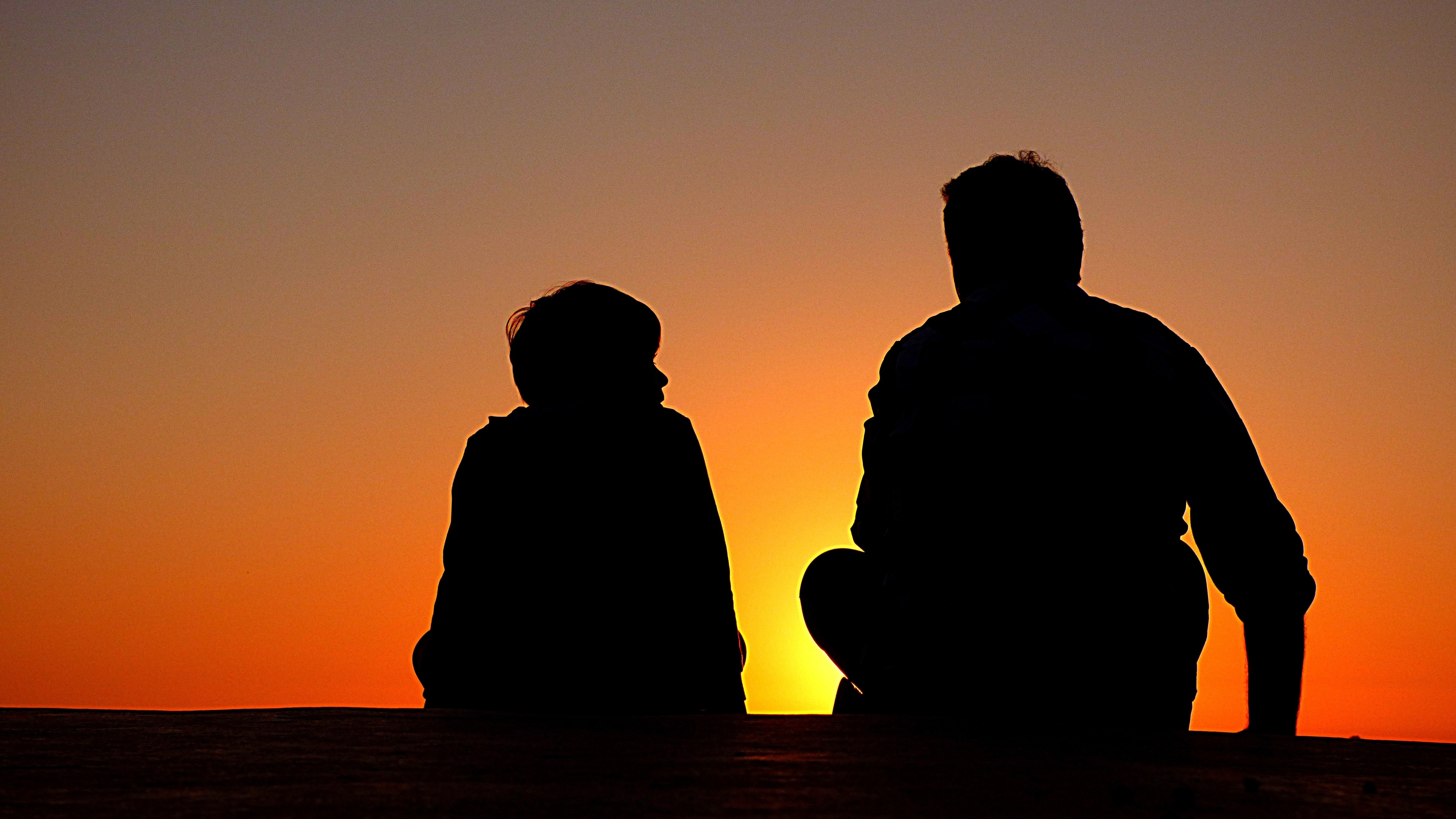 silhouette of boy and man sitting facing sunset