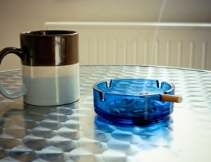 blue ashtray with lighted cigarette next to mug thumbnail