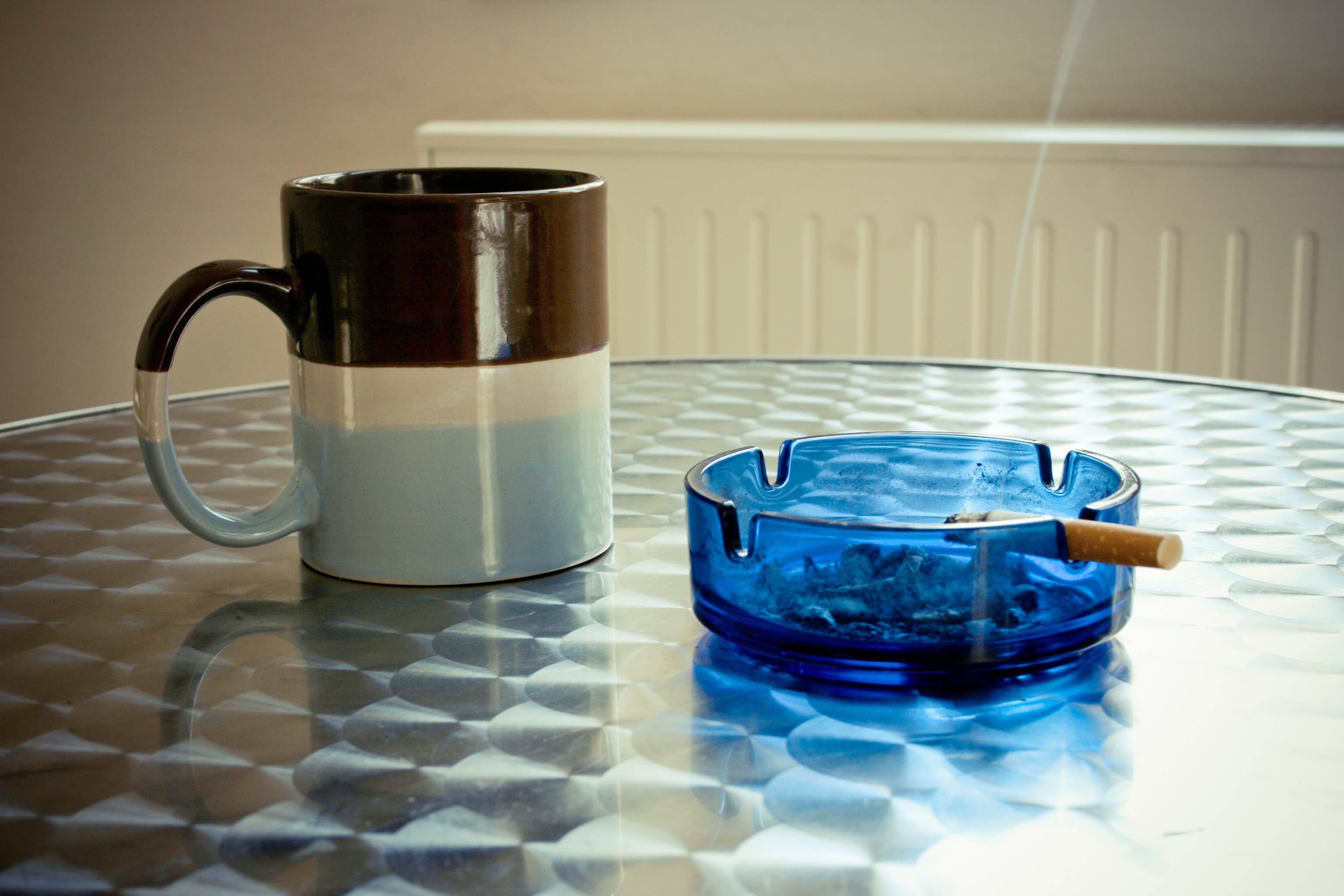 blue ashtray with lighted cigarette next to mug