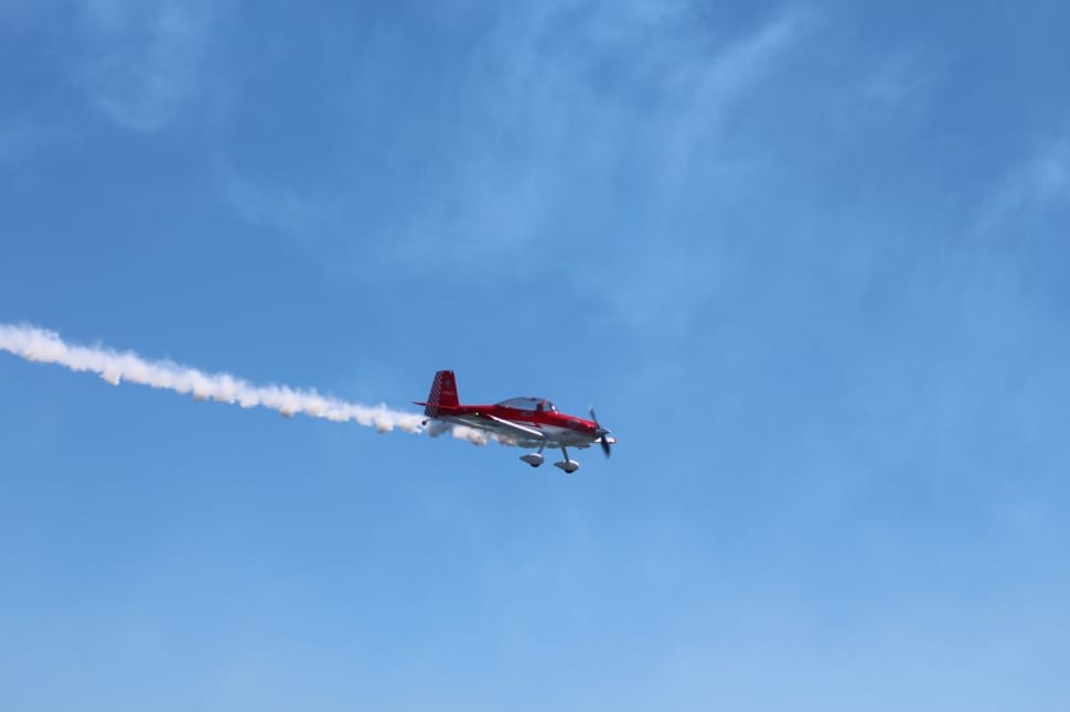 red and white biplane with tail smoke in flight during daytime preview