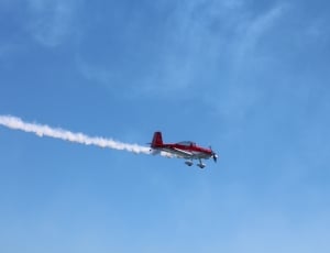 red and white biplane with tail smoke in flight during daytime thumbnail