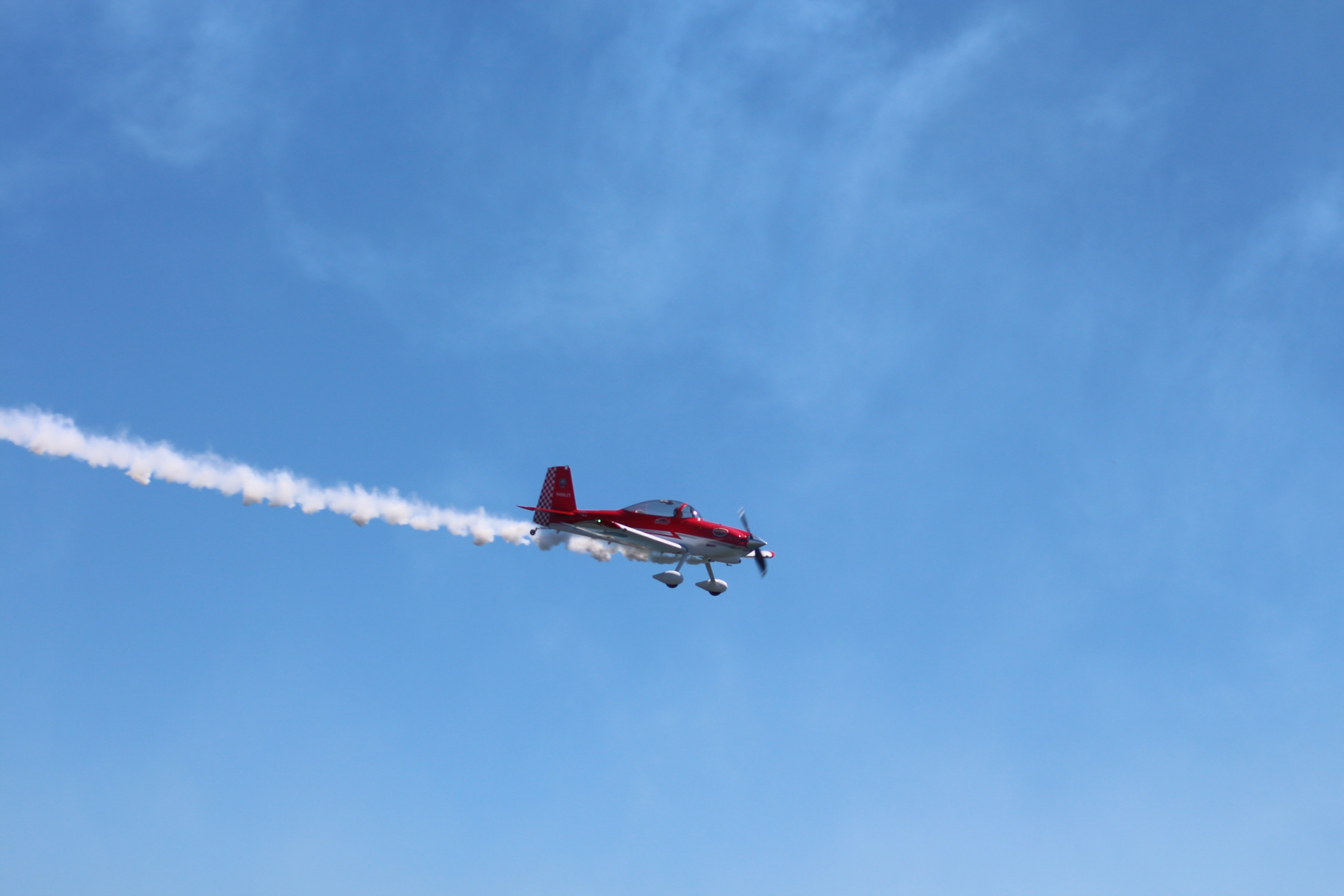 red and white biplane with tail smoke in flight during daytime