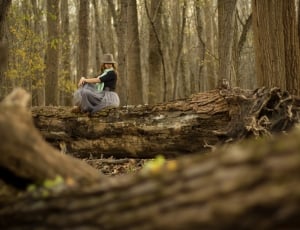woman in black shirt and grey skirt sitting on tree during daytime thumbnail