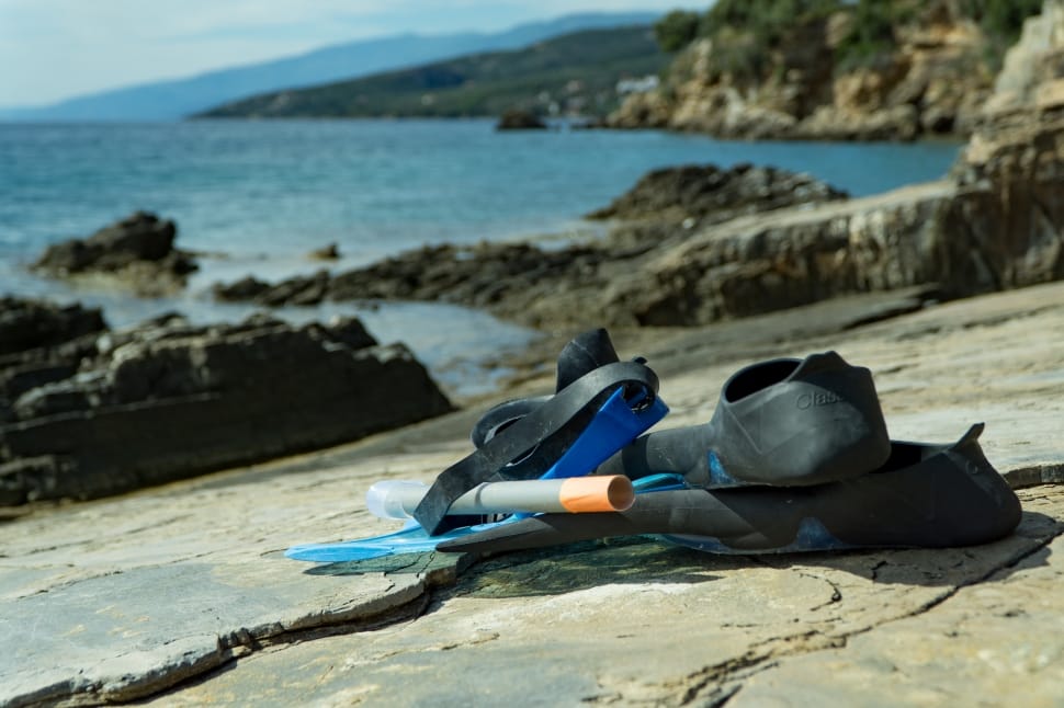 blue goggles, snorkel, and flipper on grey rock near ocean shoreline preview