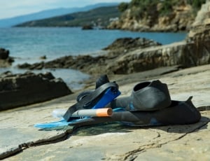blue goggles, snorkel, and flipper on grey rock near ocean shoreline thumbnail