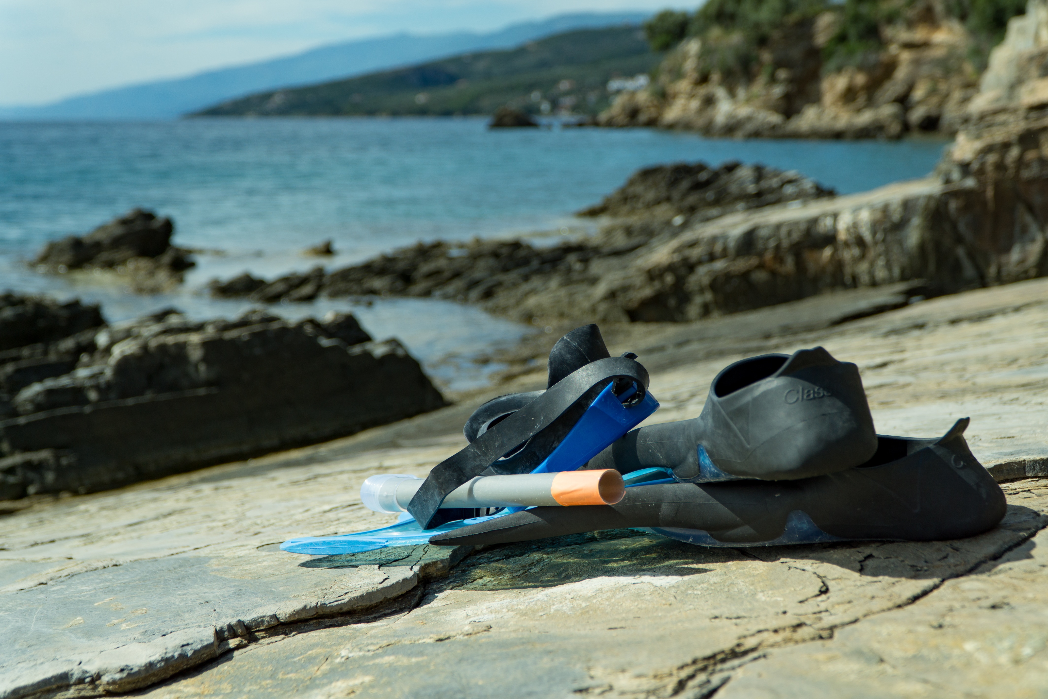 blue goggles, snorkel, and flipper on grey rock near ocean shoreline