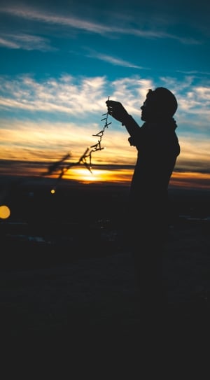 silhouette of man standing holding string lights during golden hour thumbnail