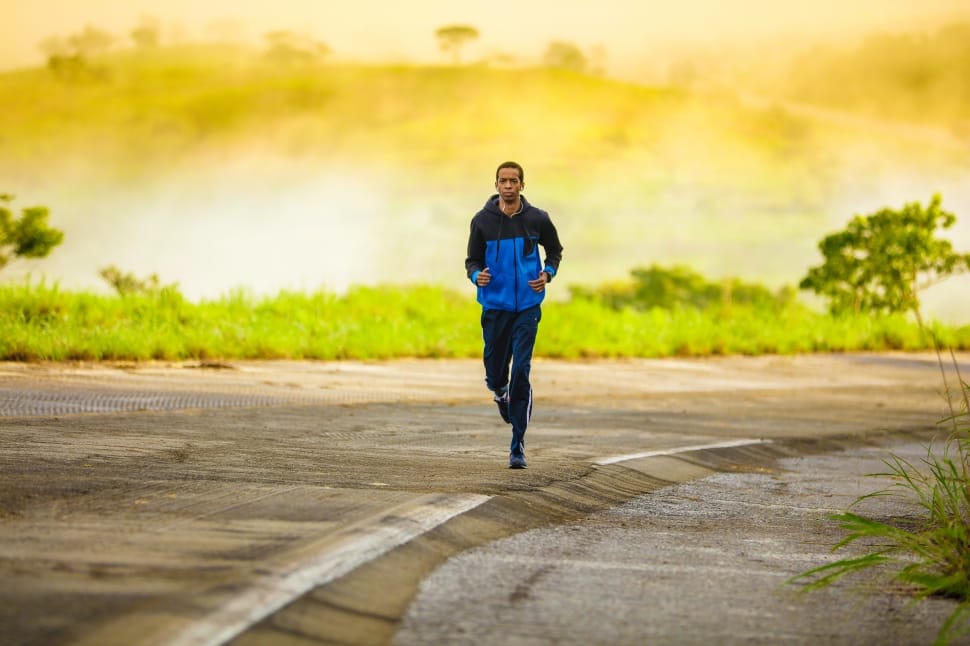 man in blue and black jacket and black track pants running on road preview