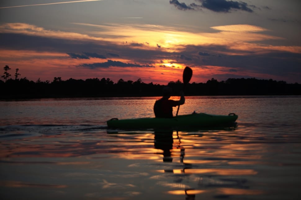 silhouette of man riding on canoe boat holding paddle during golden hour preview