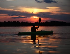 silhouette of man riding on canoe boat holding paddle during golden hour thumbnail